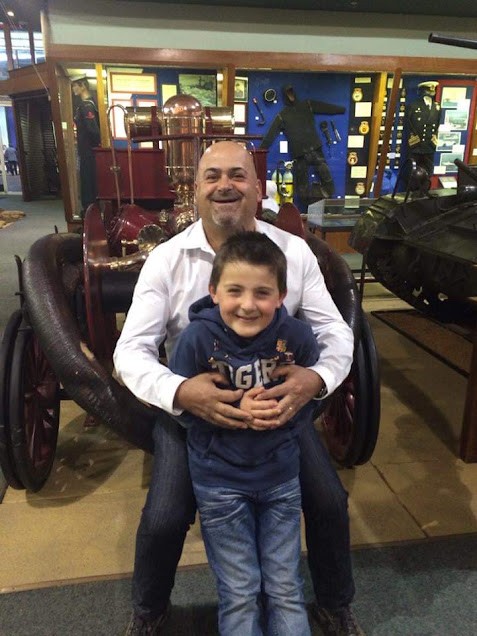 Dad smiling with his young son sitting in front of him